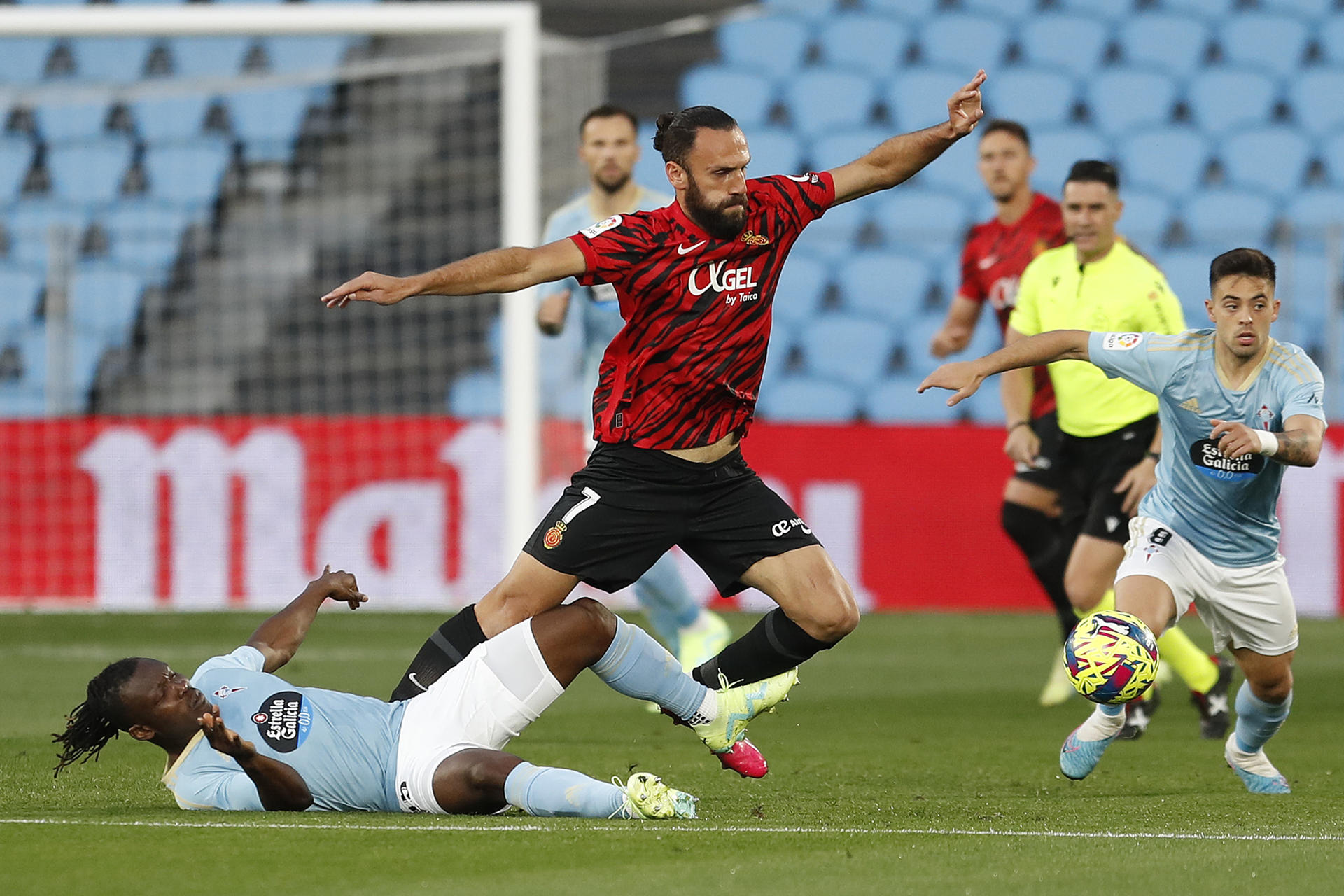 El delantero albanés del Mallorca, Vedat Muriqi (c), cae ante la entrada del defensa ghanés del Celta, Joseph Aidoo, durante el encuentro correspondiente a la jornada 29 de primera división en el estadio de Balaidos, en Vigo. EFE / Salvador Sas. 