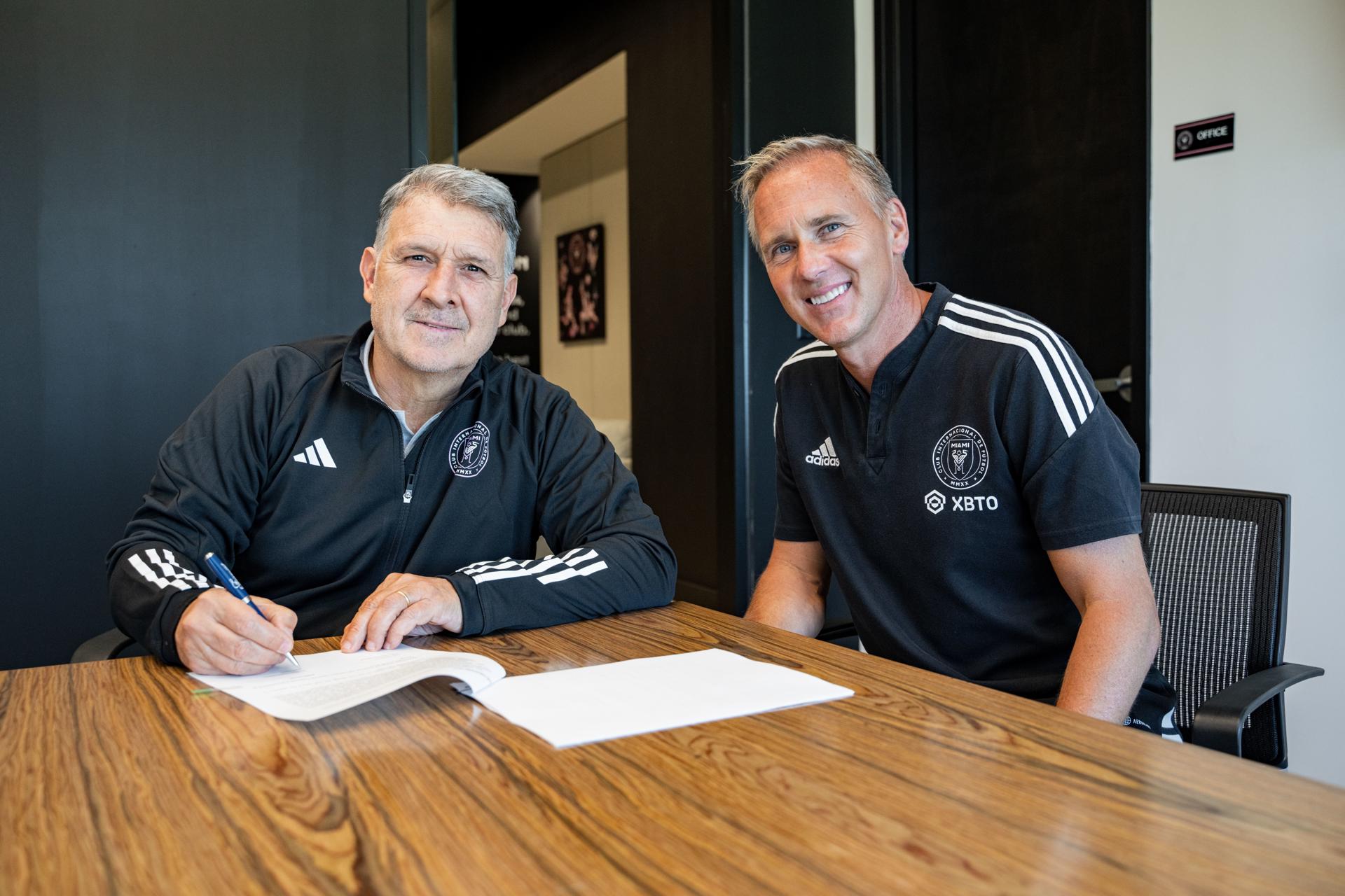 Fotografía cedida hoy por el Inter Miami CF que muestra a su nuevo entrenador, el argentino Gerardo 'Tata' Martino mientras firma acompañado por el director deportivo del club, Chris Henderson (d). EFE/Inter Miami CF 