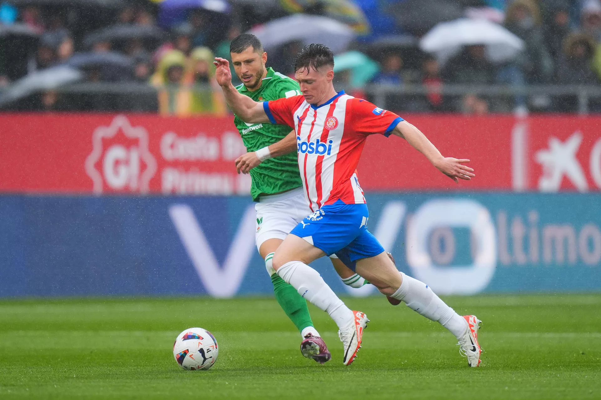 El delantero ucraniano del Girona Viktor Tsygankov disputa un balón ante el centrocampista del Betis Guido Rodríguez (i), durante el partido de la jornada 30 de LaLiga EA Sports entre el Girona y el Betis, este domingo en el estadio de Montilivi en Girona.-EFE/ Siu Wu 