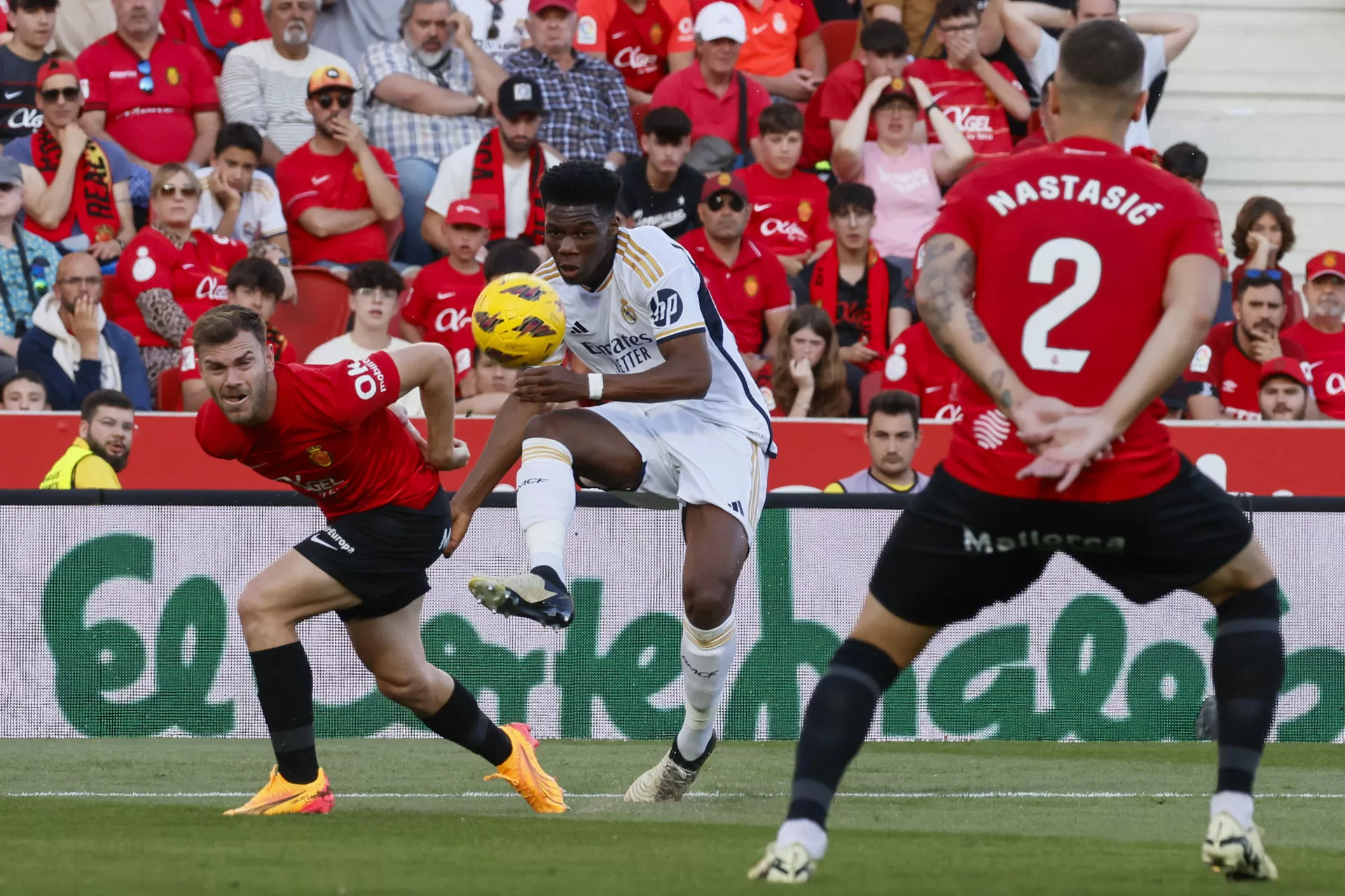 El centrocampista francés del Real Madrid, Aurelien Tchouameni (c), golpea el balón ante el defensa del Mallorca, Lato, durante el encuentro correspondiente a la jornada 31 de primera división en el estadio de Son Moix, en la capital balear. EFE/Cati Cladera. 