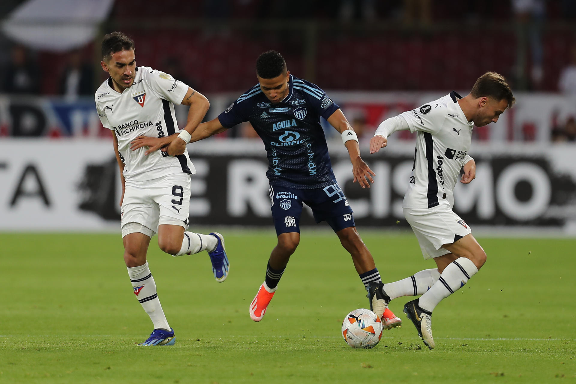 El delanteto del Junior de Barranquilla José Enamorado (c) disputa el balón con dos rivales de Liga de Quito, en un pasaje del partido de la quinta jornada del Grupo E de la Copa Libertadores jugado este martes en el estadio Rodrigo Paz Delgado de la capital ecuatoriana. EFE/ José Jácome 