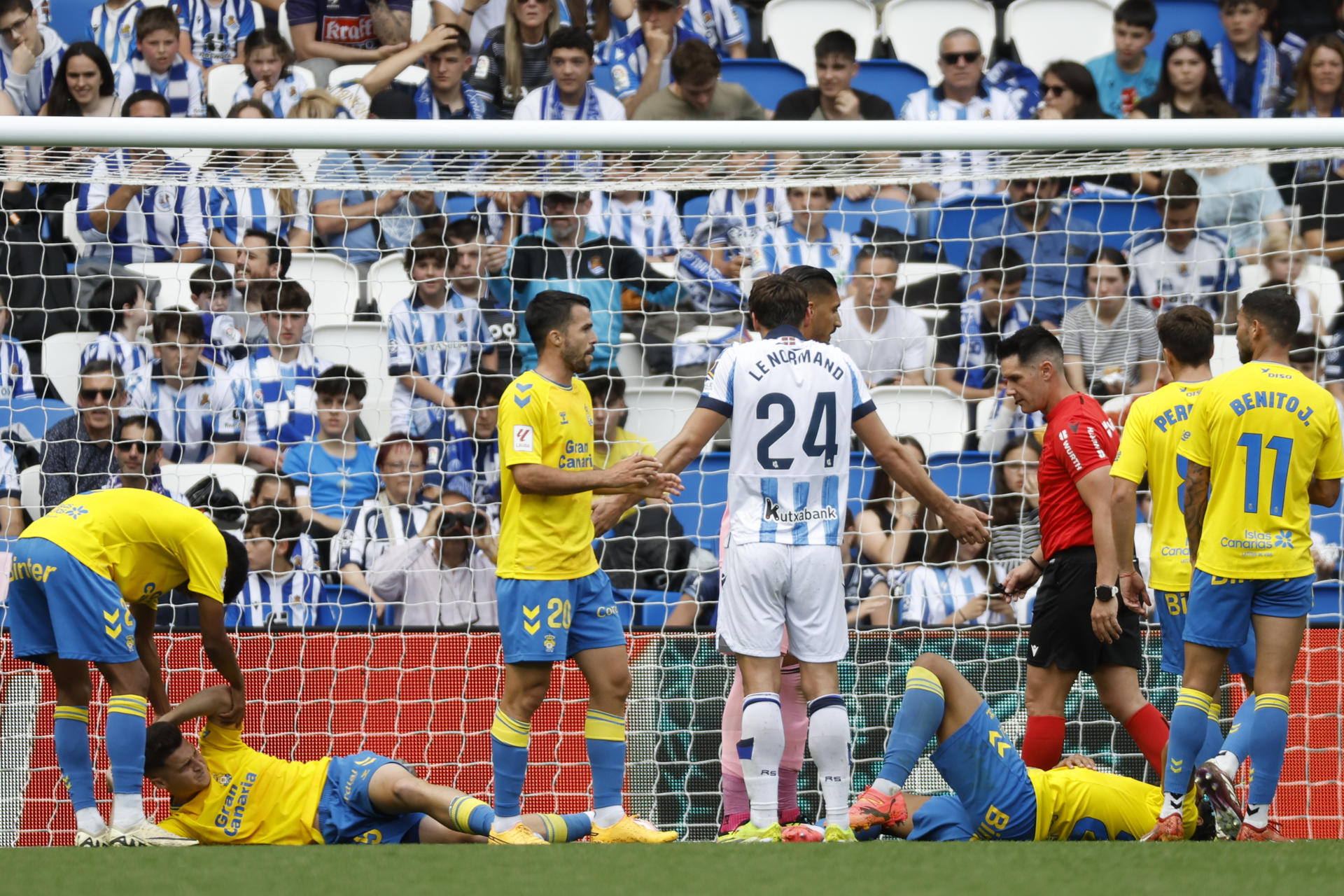 El defensa de la Real Sociedad Robin Le Normand (c) gesticula mientas dos jugadores de la UD Las Palmas se lamentan en el suelo tras una jugada durante el partido de la jornada 34 de LaLiga Ea Sports disputado este sábado en el estadio Reale Arena de San Sebastián. EFE/Juan Herrero 