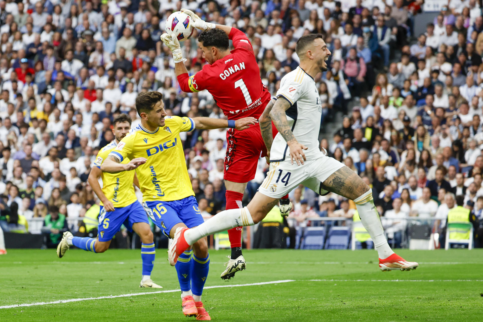 El portero del Cádiz, Conan Ledesma, se hace con el balón ante el delantero del Real Madrid Joselu Mato (d) durante el partido de la jornada 34 de la Liga EA Sports que disputan Real Madrid y Cádiz en el estadio Santiago Bernabéu en Madrid. EFE/JJ Guillén 