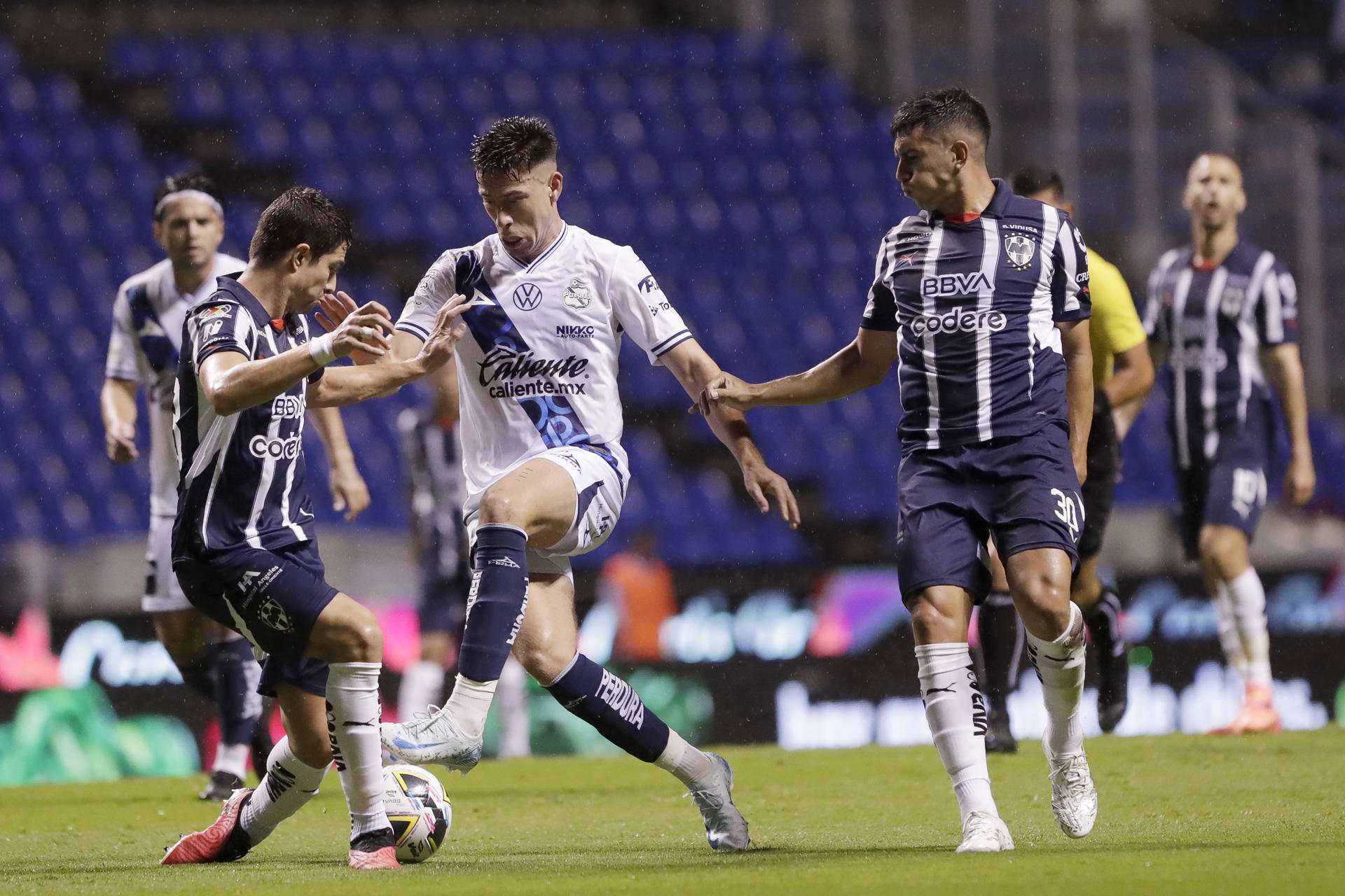 Santiago Ormeño (c) de Puebla disputa el balón con Jhon Medina (i) y Jorge Rodríguez (d) de Monterrey, este viernes durante un partido de la jornada 16 del torneo mexicano de fútbol, en el estadio Cuauhtémoc, en Puebla (México). EFE/ Hilda Ríos 
