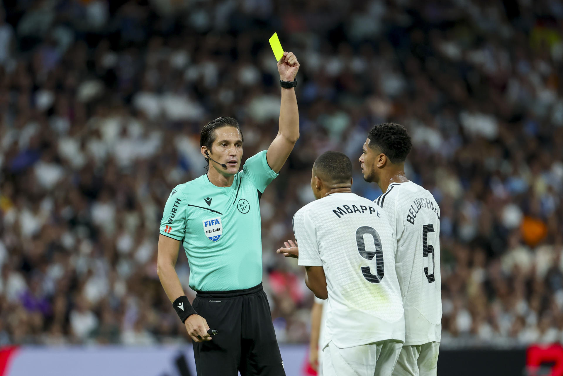 El árbitro José Luis Munuera Montero muestra la tarjeta amarilla al delantero francés del Real Madrid Kylian Mbappé (2d) durante el encuentro correspondiente a la sexta jornada de Laliga EA Sports en el estadio Santiago Bernábeu, en Madrid. EFE/Kiko Huesca.