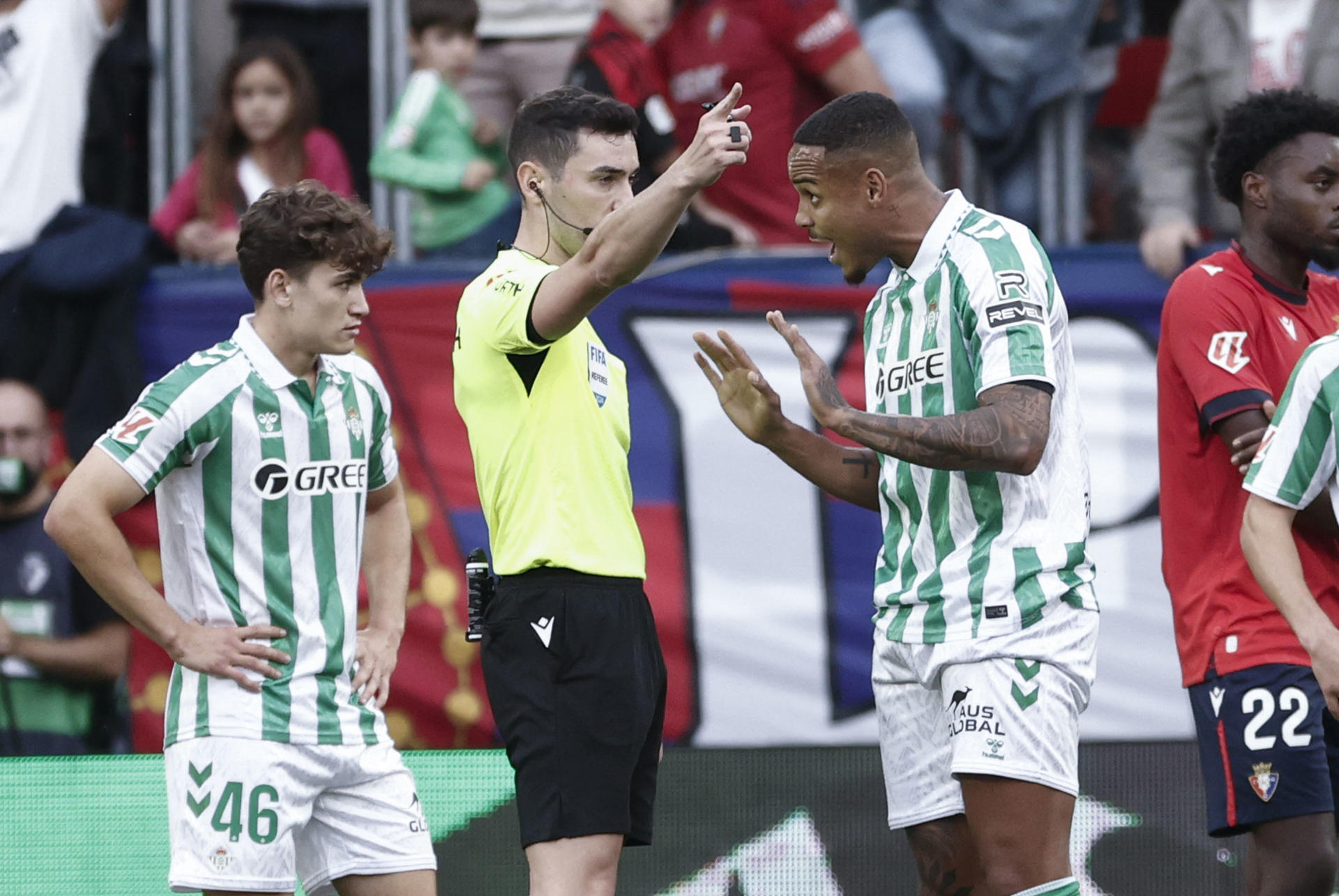El árbitro Muñiz Ruiz (c) expulsa al defensa brasileño del Betis Nathan durante el encuentro correspondiente a la décima jornada de LaLiga entre el Osasuna y el Betis en El Sadar, Pamplona, Navarra, este sábado. EFE/ Jesús Diges 