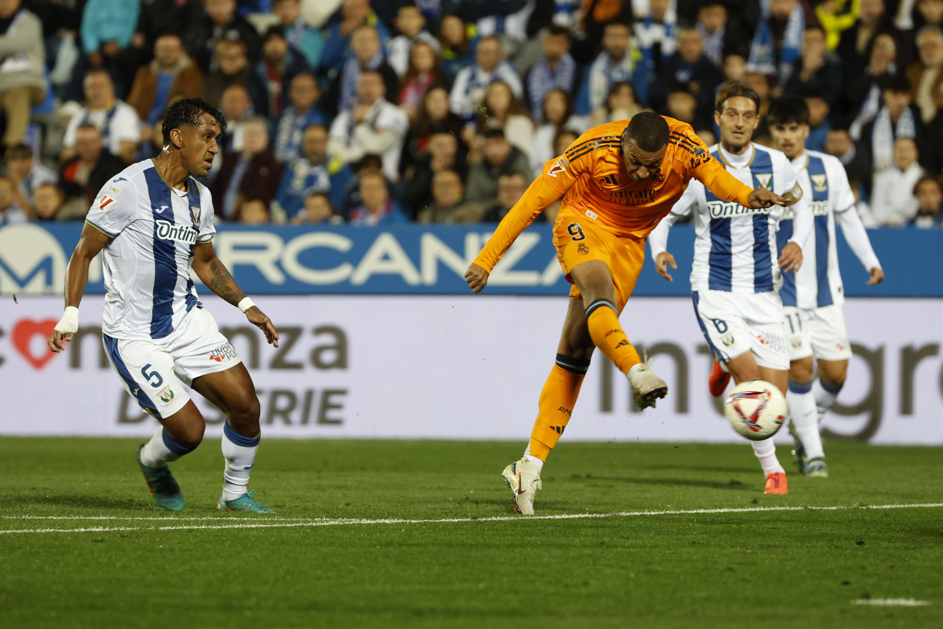 El delantero francés del Real Madrid, Kylian Mbappé (c), remata ante los jugadores del Leganés durante el encuentro correspondiente a la jornada 14 de Laliga EA Sports disputado Leganés y Real Madrid en el estadio de Butarque, en Leganés. EFE / J.J. Guillen. 