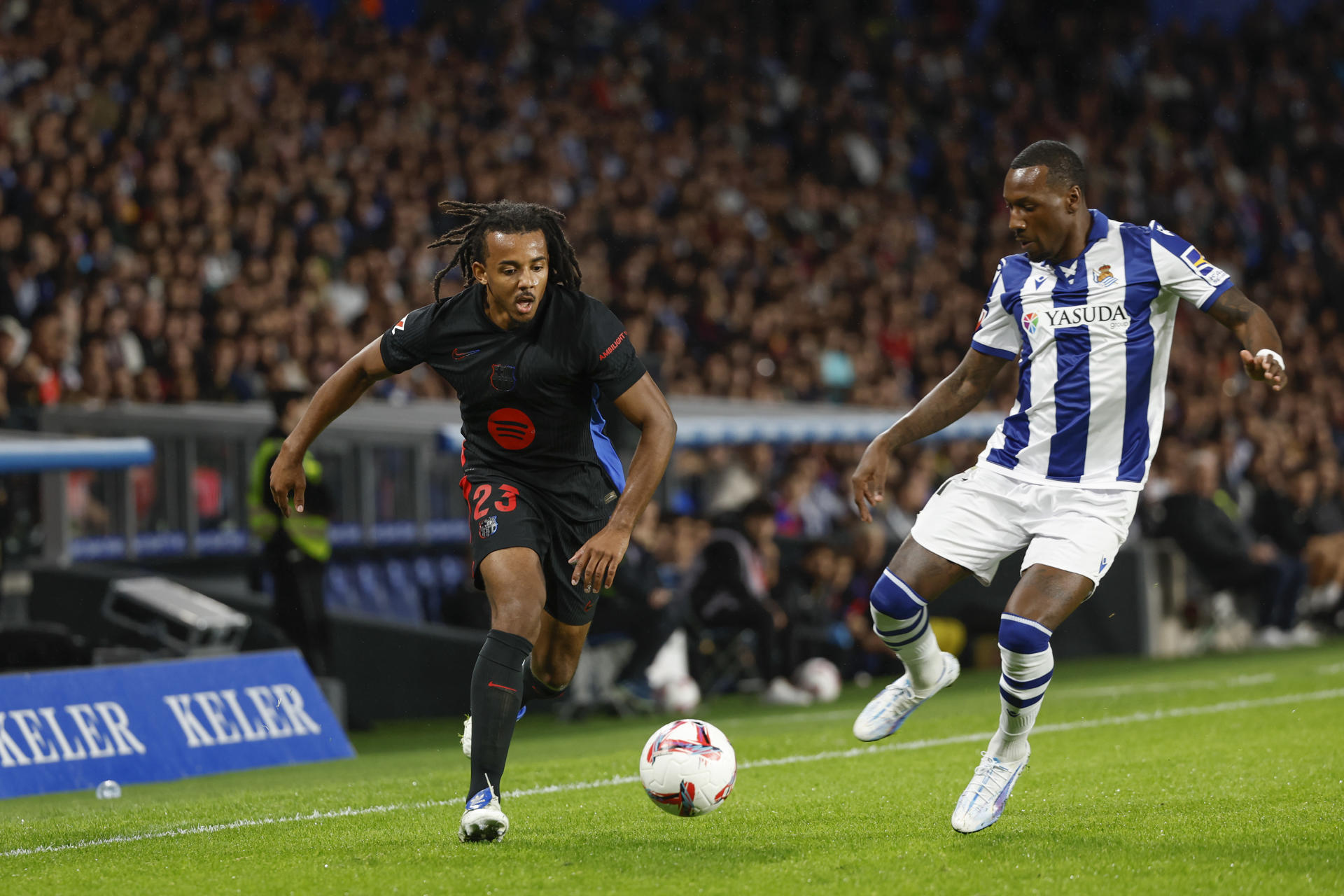 El lateral del Barcelona Jules Koundé (i) juega un balón ante Sheraldo Becker, de la Real, durante el partido de LaLiga que Real Sociedad y FC Barcelona disputan este domingo en el Reale Arena, en San Sebastián. EFE/Juan Herrero 