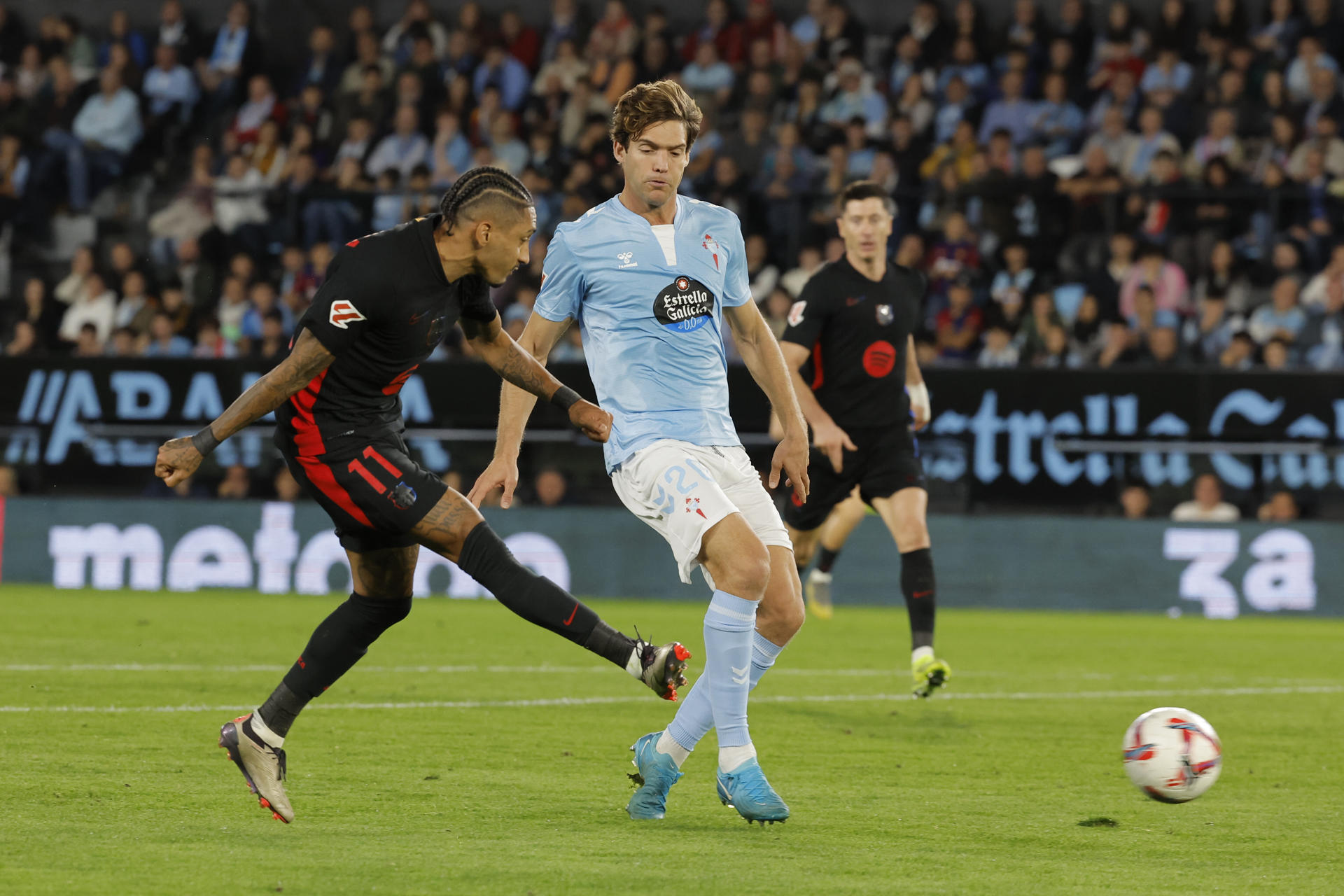 El delantero brasileño del FC Barcelona, Raphinha (i), golpea el balón ante el defensa del Celta, Marcos Alonso, durante el encuentro correspondiente a la jornada 14 de Laliga EA Sports que disputaron Celta y FC Barcelona en el estadio Balaidos de Vigo. EFE / Emilio Lavandeira. 