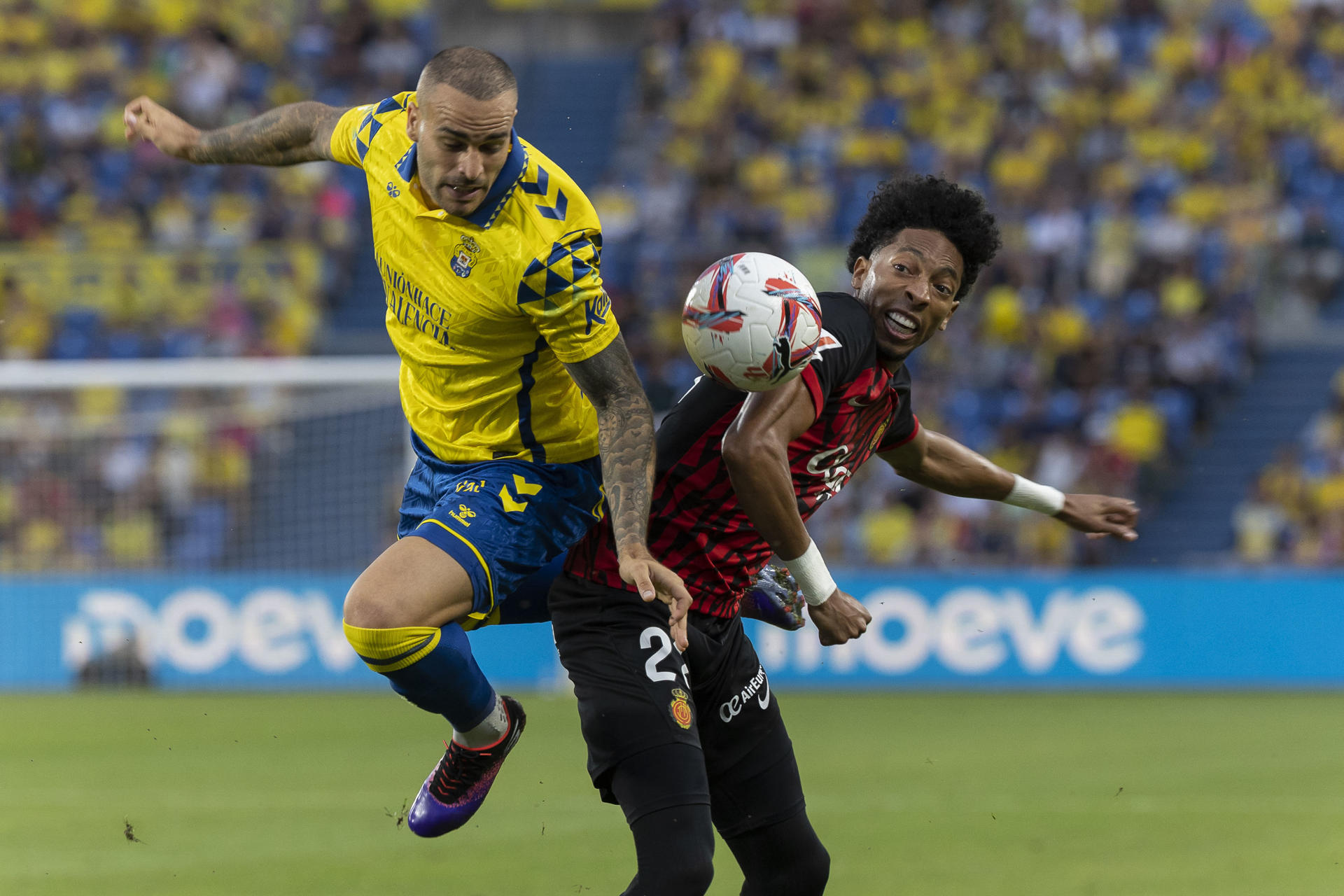 El delantero de la UD Las Palmas, Sandro Ramírez (i), disputa el balón ante el defensa colombiano del Mallorca, Mojica, durante el encuentro correspondiente a la jornada 14 de Laliga EA Sports que disputaron Las Palmas y Mallorca en el estadio de Gran Canaria. EFE/Quique Curbelo.
