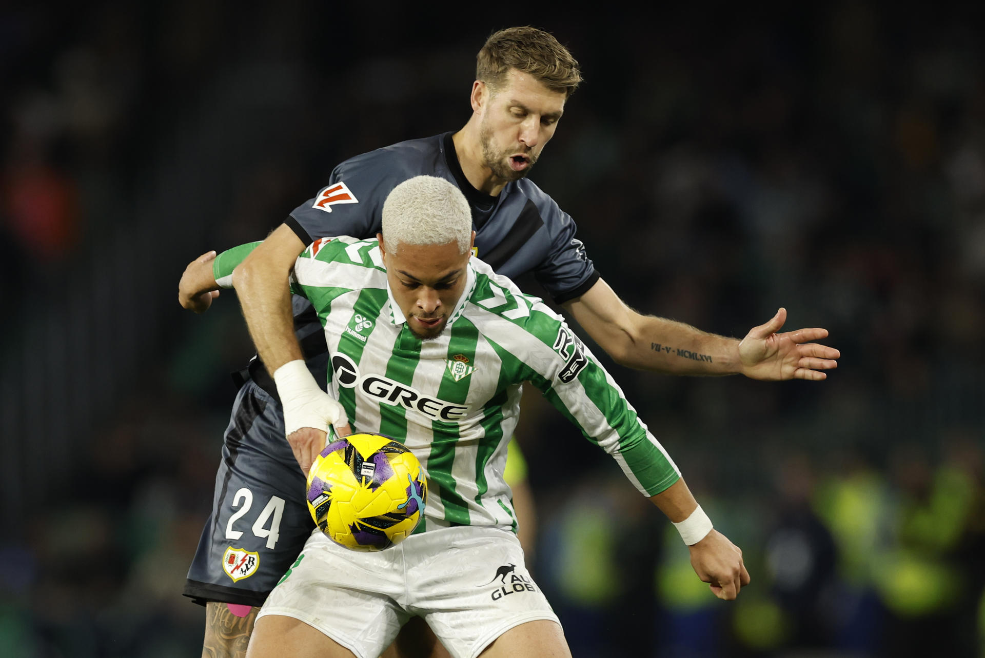 El defensa francés del Rayo Florian Lejeune (atrás) pelea una posesión con el delantero brasileño del Real Betis Vítor Roque durante el partido de la jornada 18 de LaLiga EA Sports disputado este domingo entre el Real Betis y el Rayo Vallecano en el estadio Benito Villamarín de Sevilla. EFE/ Julio Muñoz 