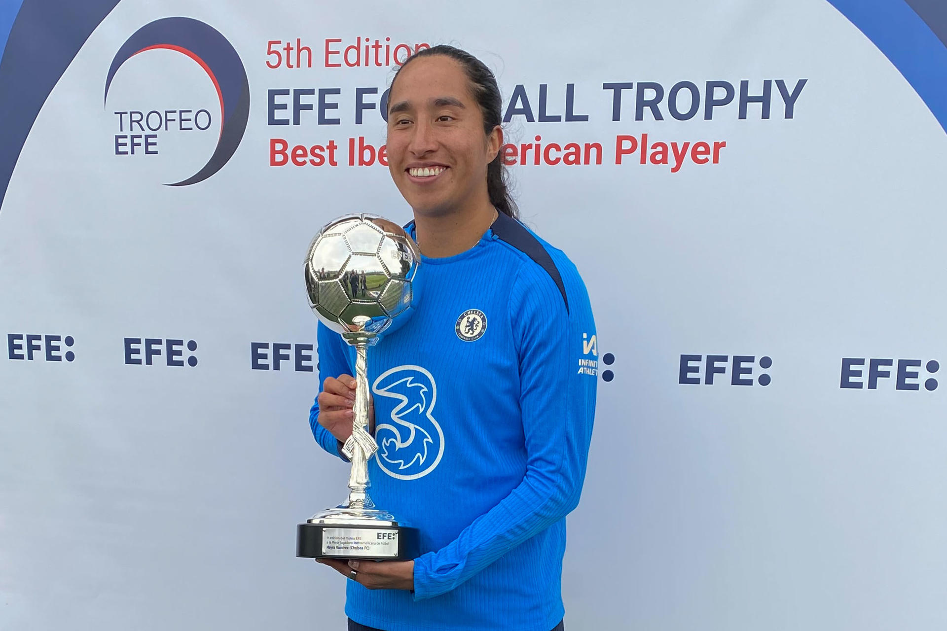 Mayra Ramírez (c), delantera colombiana del Chelsea FC, recibió este viernes de manos del presidente de la Agencia EFE, Miguel Ángel Oliver, el Trofeo EFE a la mejor jugadora Iberoamericana 2024 en un acto celebrado en las instalaciones de la Ciudad Deportiva del Chelsea en Cobham, a las afueras de Londres. EFE/ Enrique Rubio 