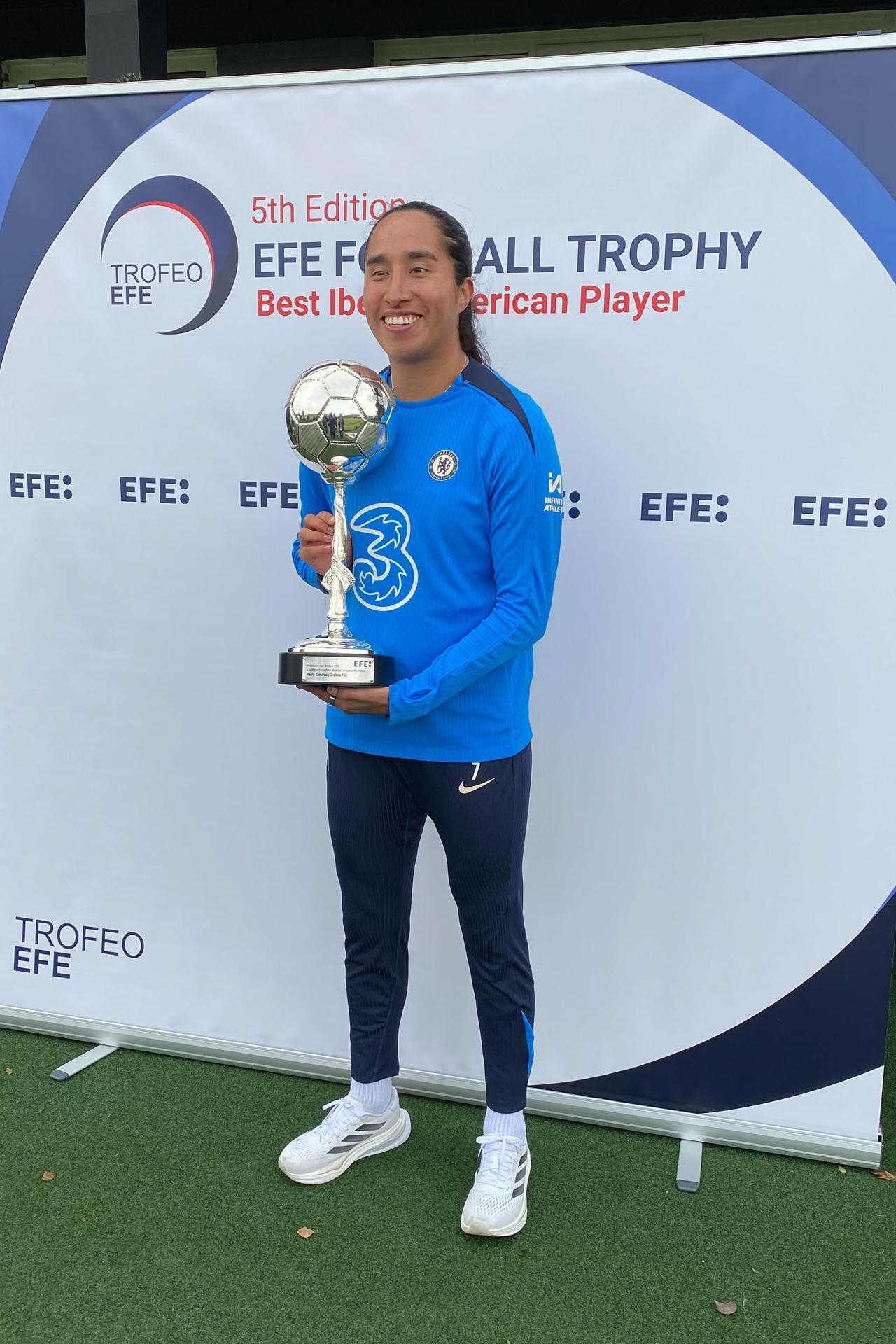 Mayra Ramírez (c), delantera colombiana del Chelsea FC, recibió este viernes de manos del presidente de la Agencia EFE, Miguel Ángel Oliver, el Trofeo EFE a la mejor jugadora Iberoamericana 2024 en un acto celebrado en las instalaciones de la Ciudad Deportiva del Chelsea en Cobham, a las afueras de Londres. EFE/ Enrique Rubio 