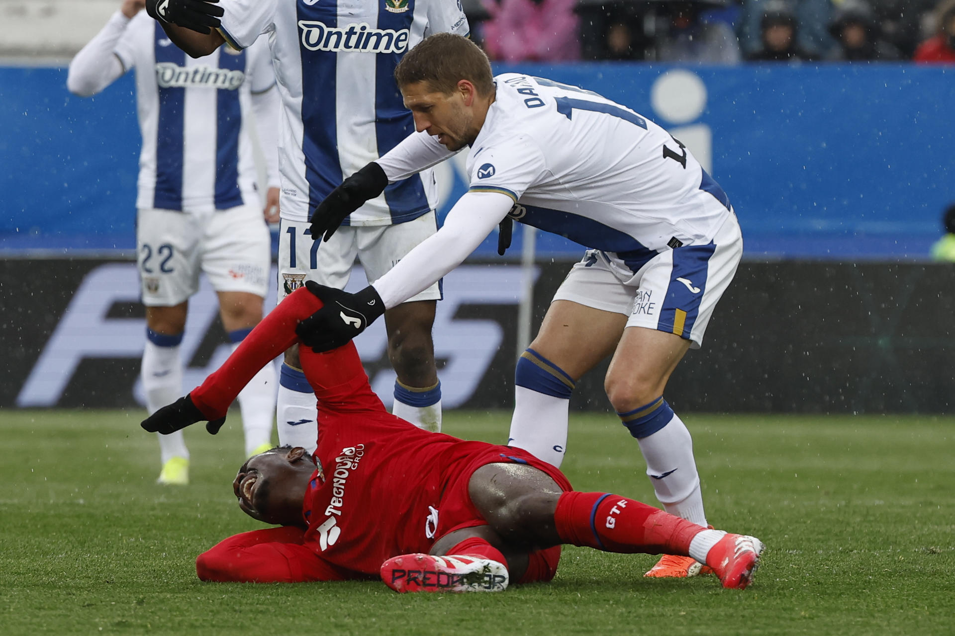 El centrocampista serbio del Leganés Darko Brašanac (d) intenta ayudar a levantarse al centrocampista del Getafe Christantus Uche (i, en el suelo) durante el partido que enfrentó al Leganés y al Getafe, este domingo, en el estadio Municipal de Butarque. EFE/Chema Moya 