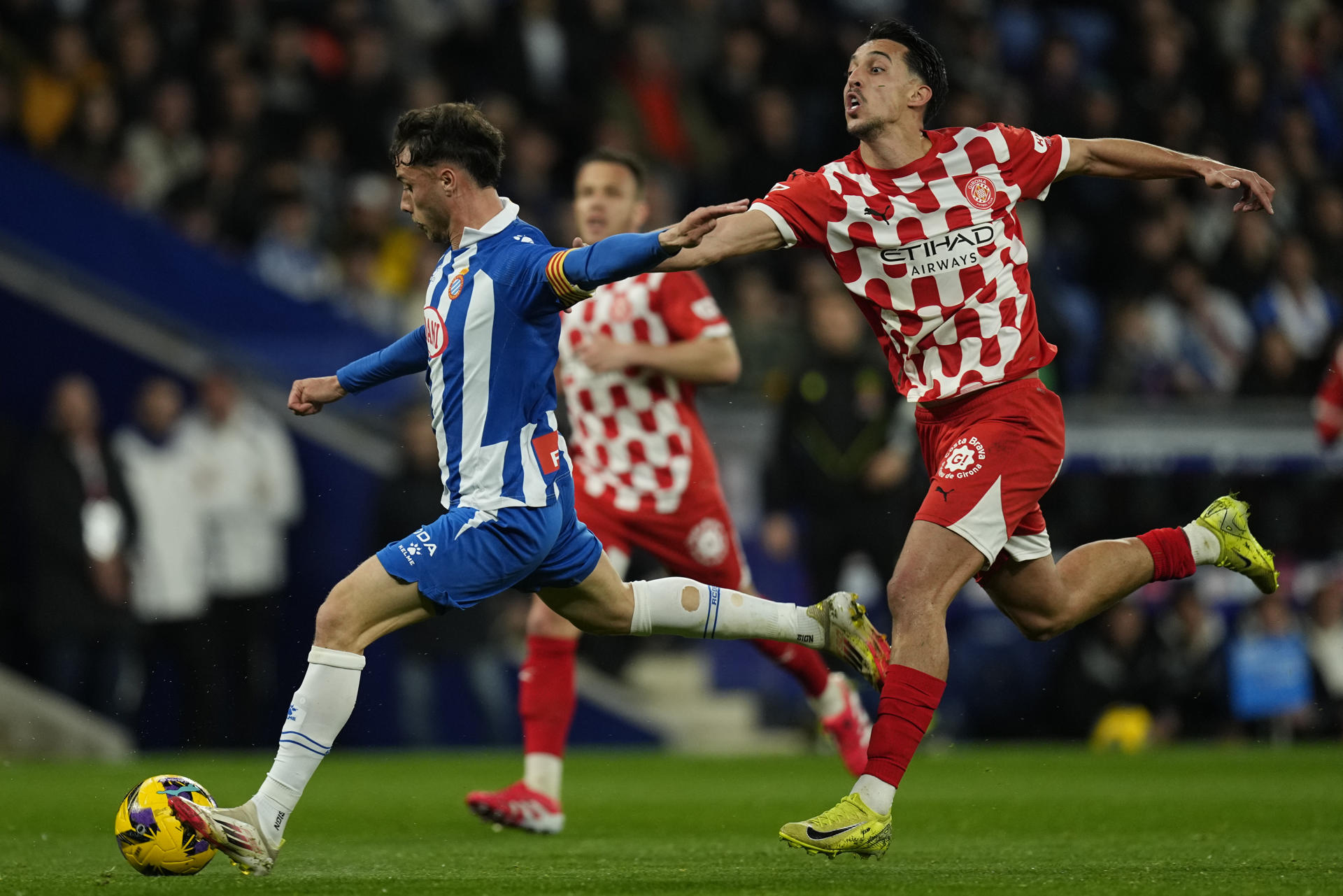 El delantero del RCD Espanyol Javi Puado (i) pelea un balón con el delantero macedonio del Girona Bojan Miovski durante el partido de la jornada 27 de LaLiga que RCD Espanyol y Girona FC disputan en el RCDE Stadium. EFE/Enric Fontcuberta 