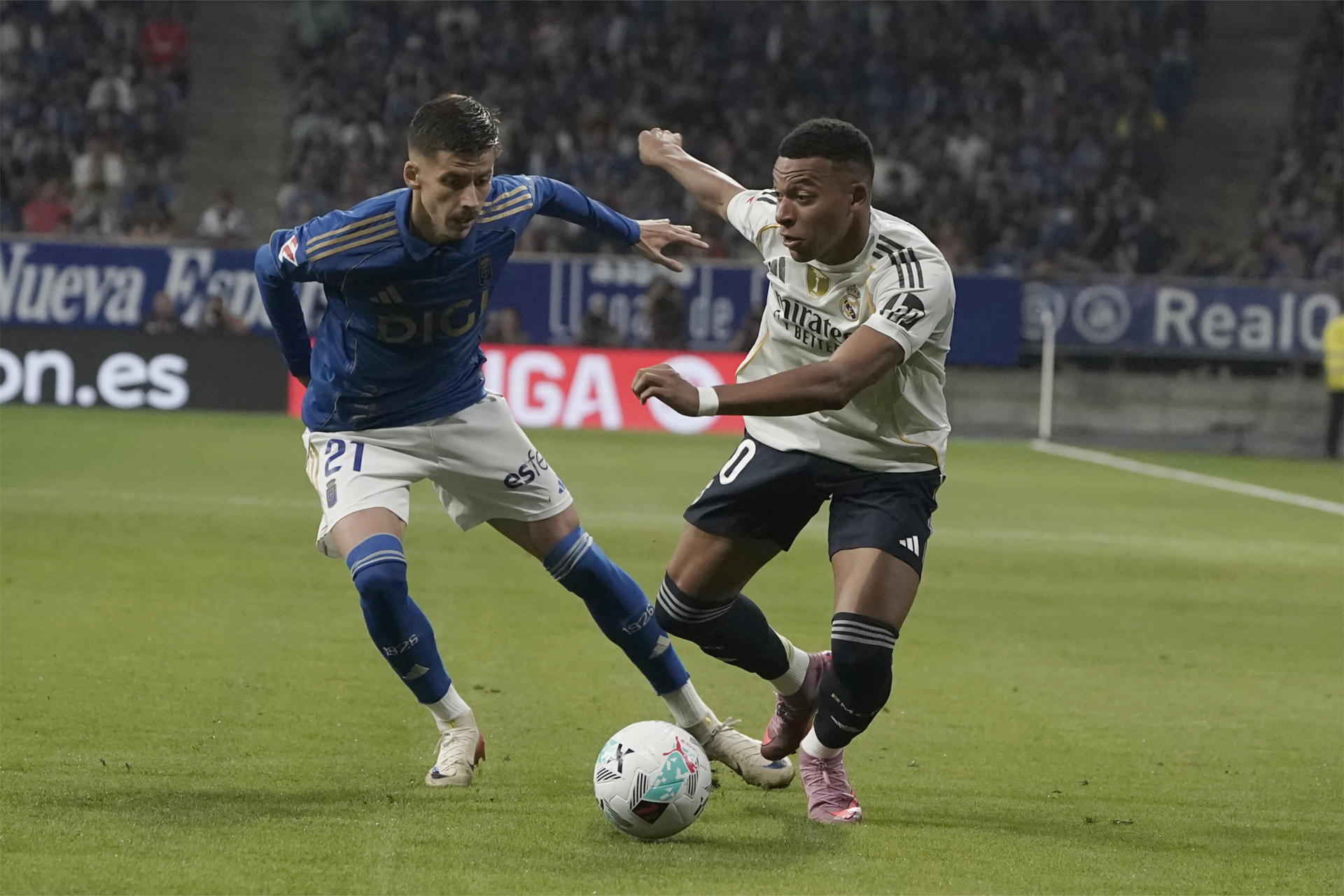 El delantero francés del Real Madrid Kylian Mbappé (d) pelea un balón con el centrocampista serbio del Real Oviedo Luka Ilic durante el partido de LaLiga que enfrenta al Real Oviedo y al Real Madrid este domingo en el estadio Carlos Tartiere. EFE/Paco Paredes 
