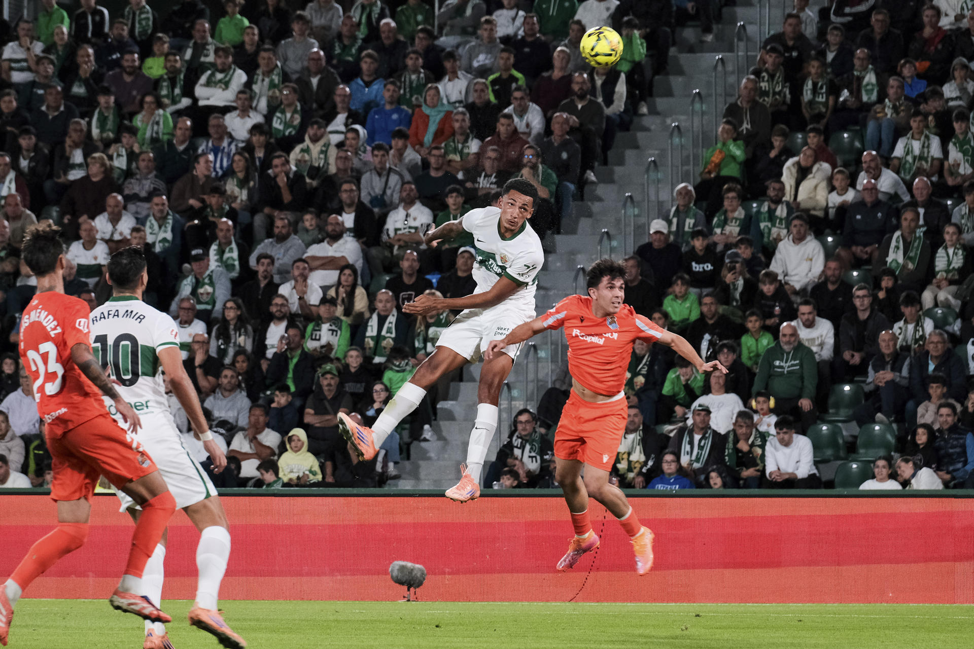 El delantero del Elche, Álvaro Rodriguez (2d), cabecea el balón ante el defensa de la Real Sociedad, Jon Aramburu, durante el encuentro correspondiente a la jornada 12 de Laliga EA Sports que disputan hoy viernes Elche y Real Sociedad en el estadio Martínez Valero de la localidad alicantina. EFE / Pablo Miranzo. 
