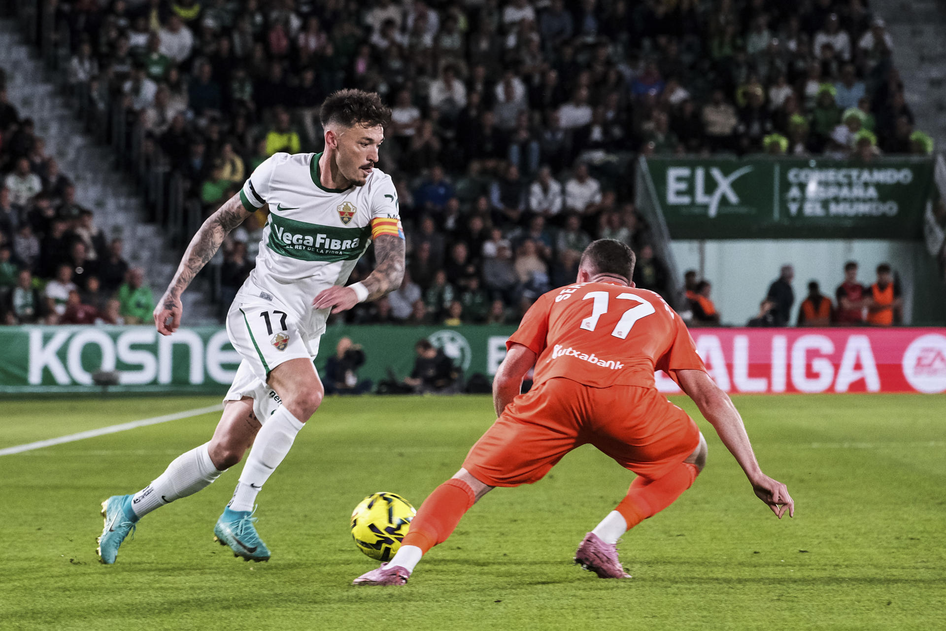 El centrocampista del Elche, Josan (i), con el balón ante el delantero de la Real Sociedad, Sergio Gómez, durante el encuentro correspondiente a la jornada 12 de Laliga EA Sports que disputan hoy viernes Elche y Real Sociedad en el estadio Martínez Valero de la localidad alicantina. EFE / Pablo Miranzo. 