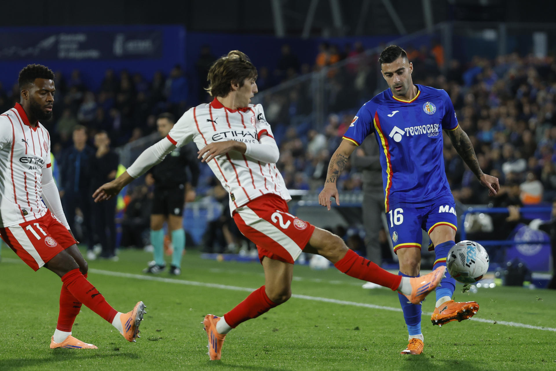 El defensa del Getafe Diego Rico (d) lucha con Bryan Gil (c), del Girona, durante el encuentro correspondiente a la jornada 11 de LaLiga EA Sports que Getafe y Girona disputan hoy viernes en el Coliseum de Getafe. EFE / Juanjo Martín.