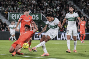 El delantero del Elche, Álvaro Rodriguez (2d), golpea el balón ante el defensa de la Real Sociedad, Jon Aramburu, para conseguir el primer gol del equipo ilicitano durante el encuentro correspondiente a la jornada 12 de Laliga EA Sports que disputan hoy viernes Elche y Real Sociedad en el estadio Martínez Valero de la localidad alicantina. EFE / Pablo Miranzo.