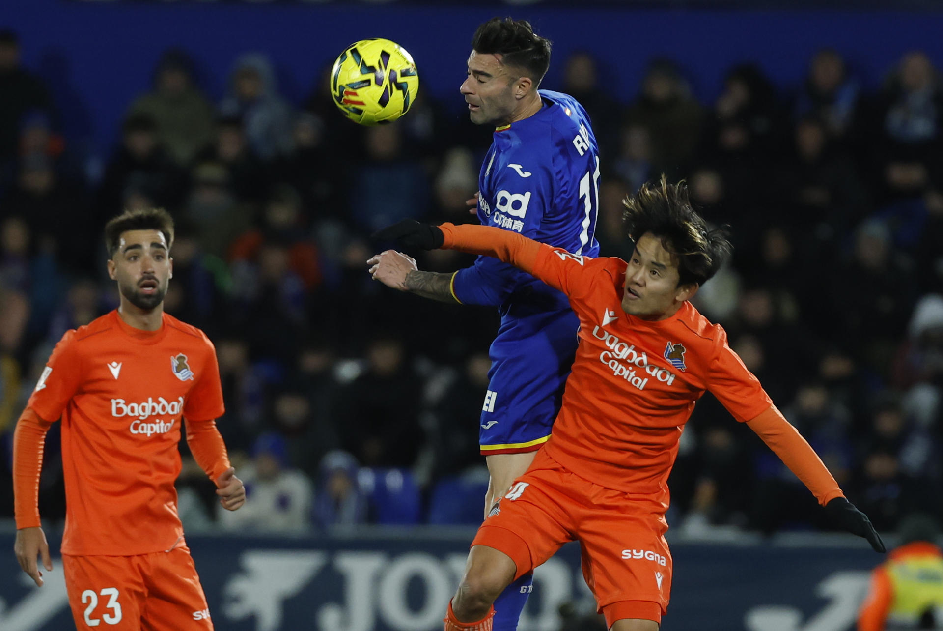 El defensa del Getafe Diego Rico (c) pelea un balón ante el centrocampista de la Real Sociedad Take Kubo (d) durante el partido de la jornada 19 de LaLiga EA Sports que disputaron Getafe CF y la Real Sociedad este viernes, en el Coliseum de Getafe (Comunidad de Madrid). EFE/ Juanjo Martín