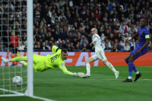 El guardameta alemán del AS Mónaco, Philipp Köhn (i), intenta detener el remate del centrocampista argentino del Real Madrid, Mastantuono, en la jugada que ha significado el tercer gol del equipo madridista durante el encuentro correspondiente a la Liga de Campeones UEFA que disputaron el Real Madrid y el AS Mónaco, en el estadio Santiago Bernabéu en Madrid. EFE/ Kiko Huesca.