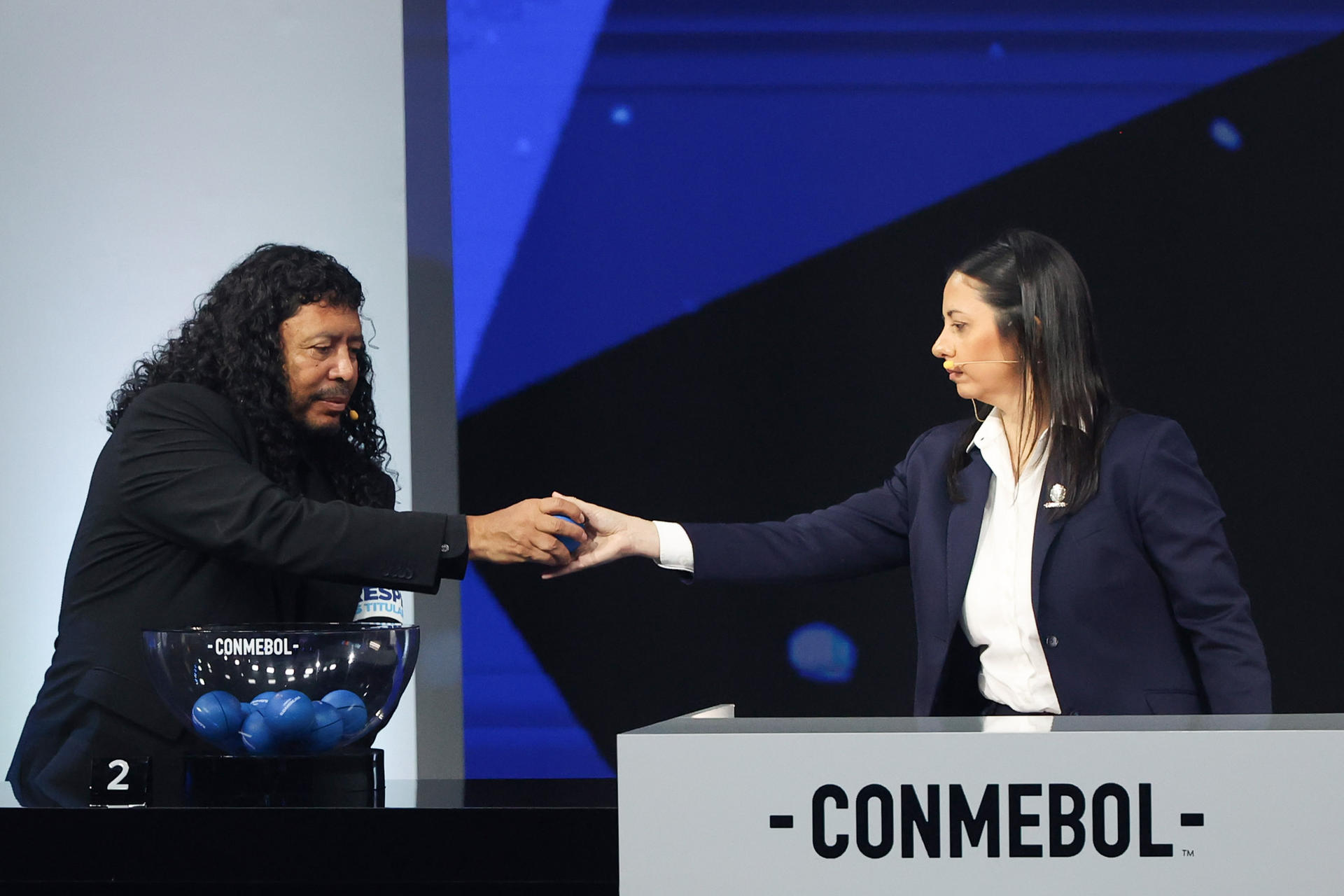 El exfutbolista colombiano René Higuita (i) entrega una balota a la gerenta de Competiciones de la Conmebol, Luciana Antunes, durante el sorteo de la fase de grupos de la Copa Sudamericana 2026 en Luque (Paraguay). EFE/Juan Pablo Pino
