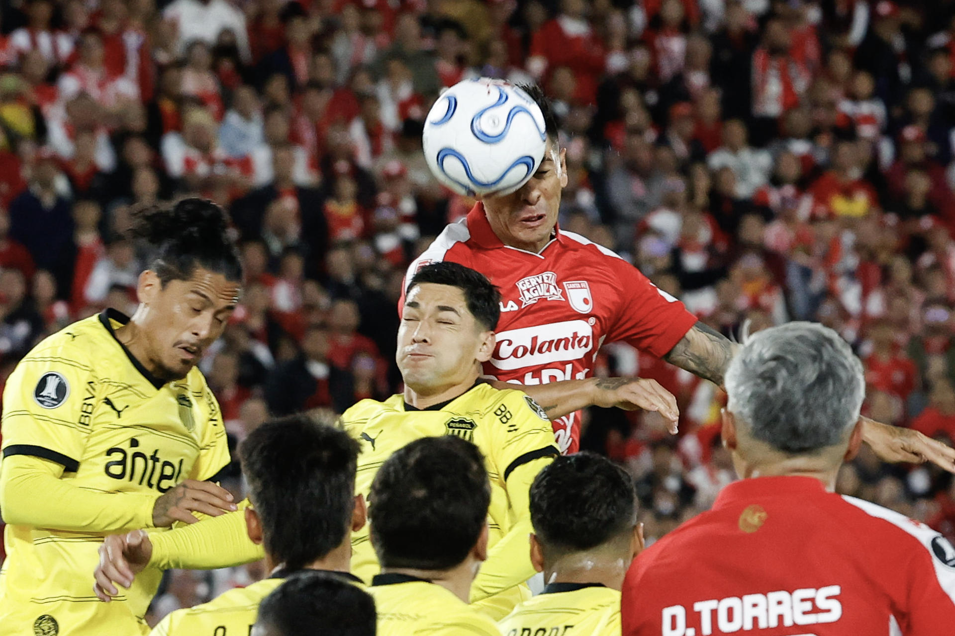 El central argentino de Independiente Santa Fe, Emmanuel Olivera (c), supera a los defensores de Peñarol al conectar un centro aéreo durante el partido que cerró este jueves la primera jornada de la fase de grupos de la Copa Libertadores en el estadio El Campín de Bogotá. EFE/ Mauricio Dueñas Castañeda
