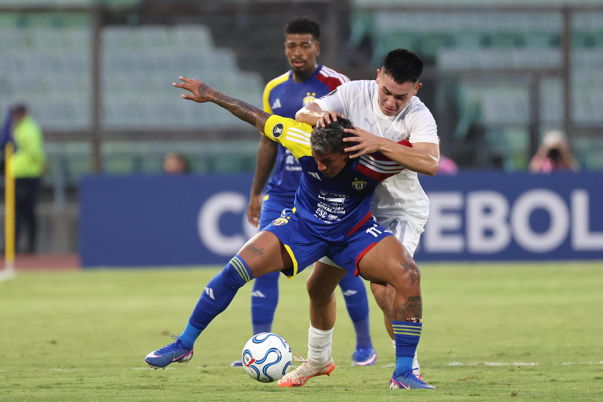 Jovanny Bolívar (c), de Universidad Central, disputa el balón con Thiago Fernandez, de Libertad, en un partido de la fase de grupos de la Copa Libertadores en Caracas. EFE/Miguel Gutiérrez
