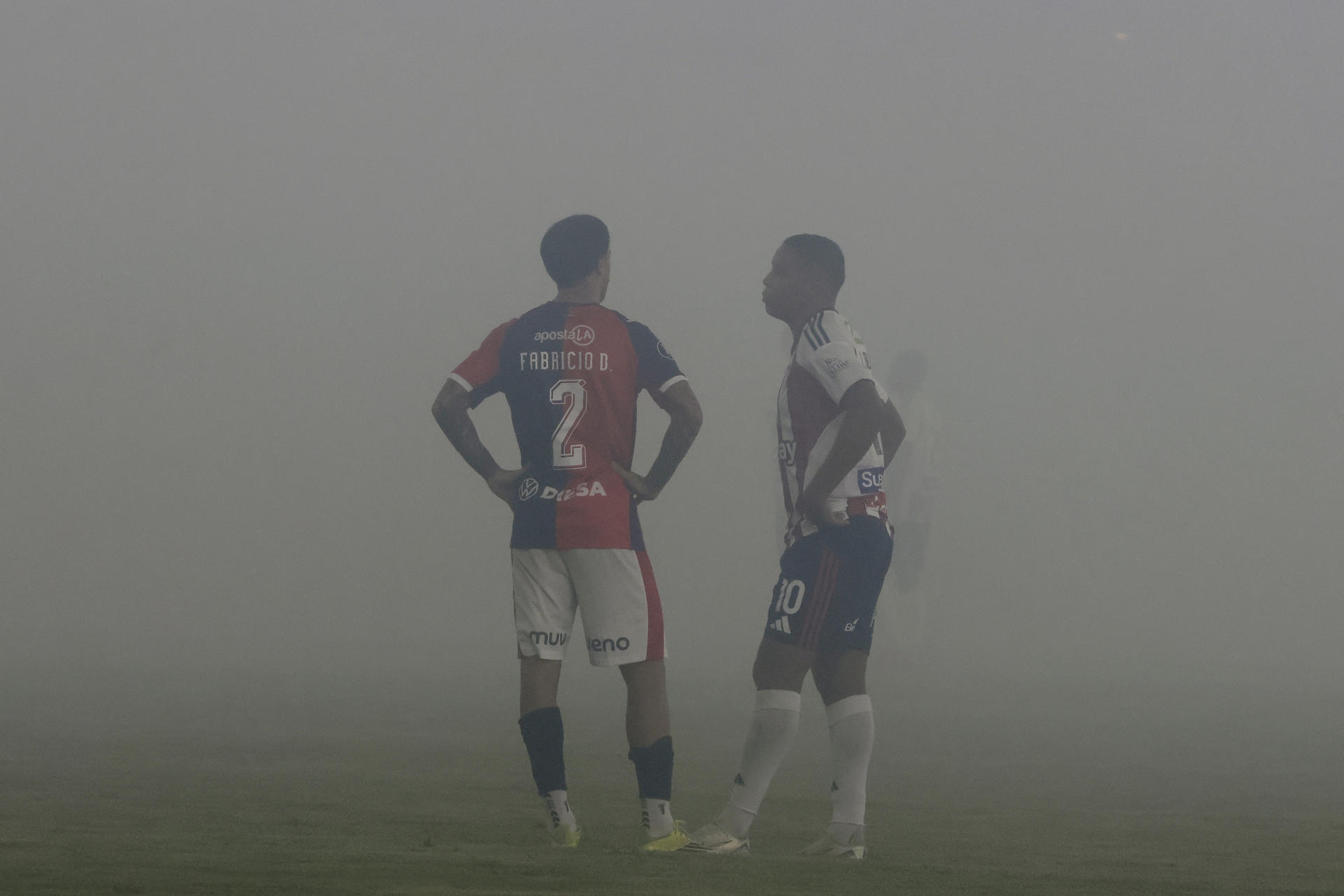 Luis Fernando Muriel (d), de Junior, y Fabricio Domínguez, de Cerro Porteño, esperan que se disipe el humo de unas bengalas en el partido de Copa Libertadores en el estadio Jaime Morón en Cartagena (Colombia). EFE/Ricardo Maldonado Rozo
