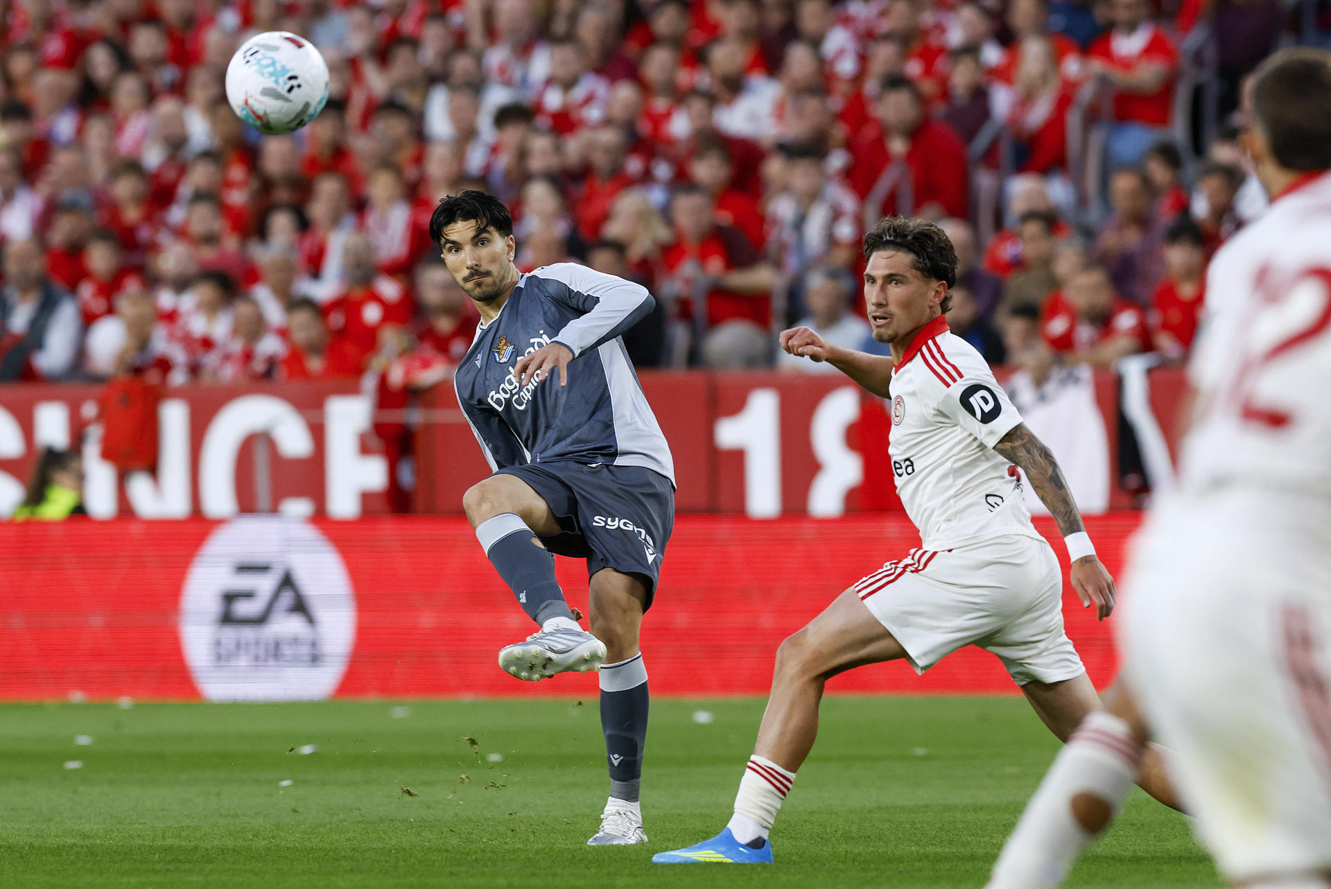 El centrocampista de la Real Sociedad Carlos Soler (i) efectúa un centro durante el partido de la jornada 34 de LaLiga EA Sports que el Sevilla FC y la Real Sociedad disputan en el estadio Ramón Sánchez-Pizjuán de la capital andaluza. EFE/ Julio Muñoz
